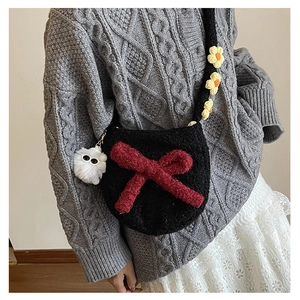 Détail du sac bandoulière en tricot noir avec nœud rouge et fleurs sur la sangle