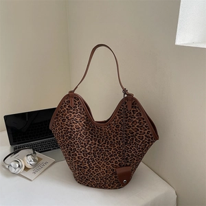 Detail of leopard print tote bag with brown leather trim next to a laptop
