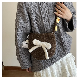 Détail d'un sac bandoulière en peluche marron avec nœud blanc et breloque mouton