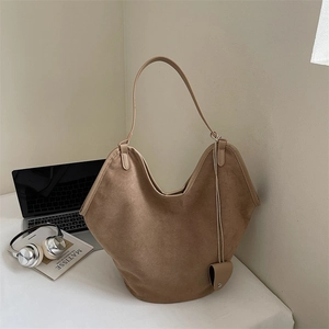 Detail of camel suede tote bag with heart charm next to a laptop and headphones