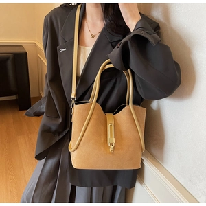 Detailed close-up of a light brown suede bucket bag featuring a gold rectangular metal lock