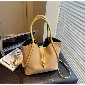 Detail of camel suede tote bag with long tubular handles and gold metal lock on a leather stool