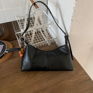 Detail der schwarzen glänzenden Baguette-Tasche aus PU-Leder mit Ziernähten und Anhänger