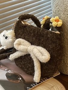 Sac bandoulière marron en peluche avec nœud crème et charm monstre dans un décor doux