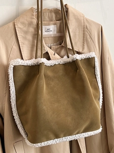 Braune Wildleder-Einkaufstasche mit weißem Plüschbesatz an einem beigen Trenchcoat