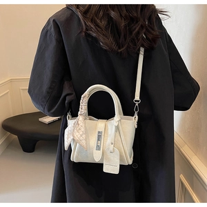 Close-up of a white leather bucket bag with a decorative silk scarf on the handle