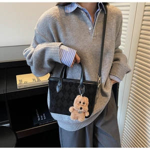 Close-up of black quilted shoulder bag with plush bear charm and textured fabric finish
