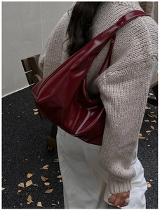 Macro shot of a vintage burgundy high-gloss leather hobo bag on a model's shoulder
