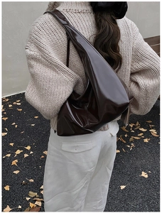 Outdoor view of a dark brown vintage patent leather tote bag styled with a cream sweater