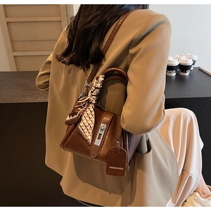 Close-up of brown leather bucket bag with metal lock and decorative silk scarf detail