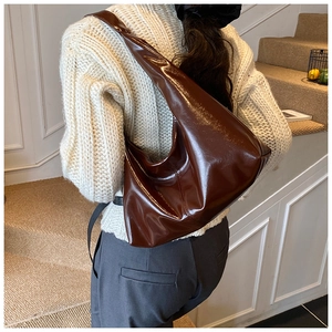 Glossy caramel brown tote bag worn over shoulder with sleek seamless strap design