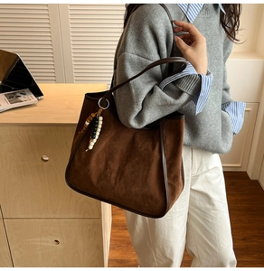 Detail of dark brown suede tote bag with leather trim and colorful beaded pendant accessory