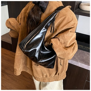 Detail of high-gloss black leather shoulder bag showing texture and drape on model