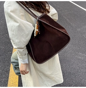 Detail of dark brown suede tote bag with decorative beaded charm on long shoulder strap