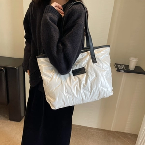 Detailed close-up of white quilted down tote bag with black leather straps and brand label