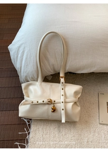 Dettaglio della borsa tote a pieghe bianco crema con fibbia dorata e ciondolo a fagiolo