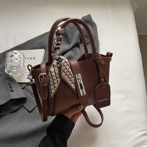 Detail of dark brown leather bucket bag with silver turn-lock and silk scarf handle