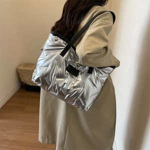 Close-up of a silver quilted puffer tote bag with black handles on a female model