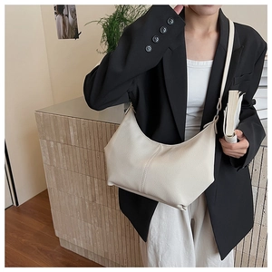 Sac à bandoulière demi-lune en cuir beige porté avec un blazer noir et un pantalon blanc