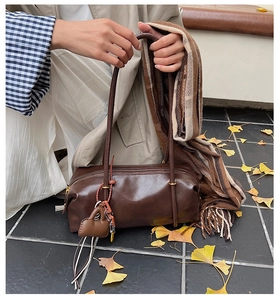 Fashionable dark brown cylindrical shoulder bag with a mini charm on autumn ginkgo leaves