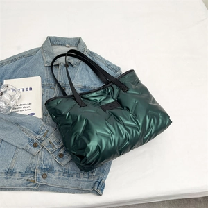 Detail of dark green quilted tote bag with black leather handles on denim