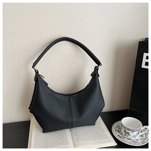 Sac sous le bras minimaliste en cuir noir mat sur un livre avec tasse de café