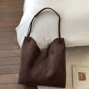 Détail d'un sac hobo en daim marron avec ouverture en V et surpiqûres verticales fines