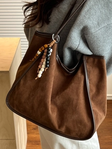 Brown suede tote bag with leather trim and beaded pendant shown in a lifestyle indoor setting