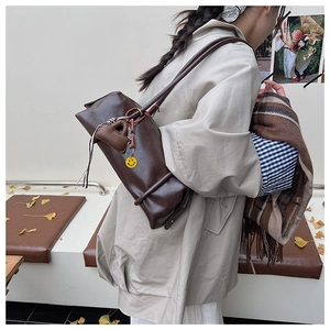 Chic brown leather shoulder bag with smiley charm on model in autumn park setting