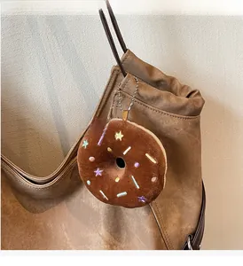 Brown plush donut charm with colorful embroidery hanging on a vintage canvas tote bag