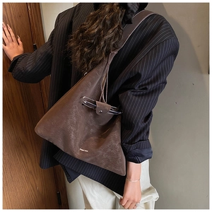 Detail of a large vintage brown suede shoulder bag with gold logo and creative glasses holder