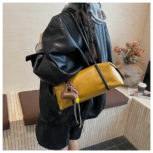 Detail of yellow cylinder pillow bag with charms worn over a black leather jacket