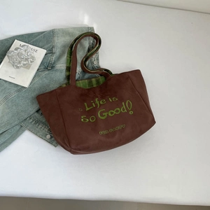 Detail der Wildleder-Tragetasche mit grüner Stickerei und karierten Riemen auf Weiß