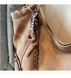 Detail of khaki tote bag featuring creative silver letter and donut charms with braided rope