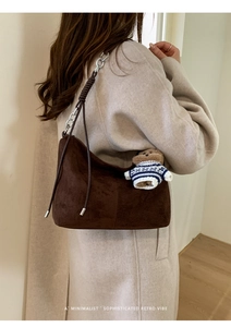Detail of suede hobo bag with chain strap and teddy bear charm on model's shoulder