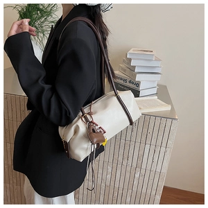 Detail view of cream white barrel bag with dark brown strap and heart charm on a side