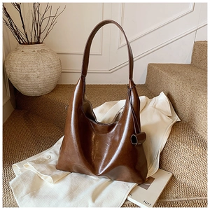 Detailed close-up of dark brown leather tote bag with stylish knot on white blazer background