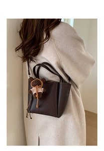Detail of dark chocolate leather tote bag with a cute woven bear charm and long strap