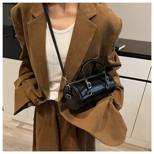 Close-up of a glossy black barrel bag worn cross-body over a vintage striped blazer