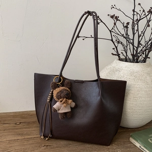 Détail du sac cabas marron foncé avec texture litchi, charm d'ours en peluche et pompon en cuir