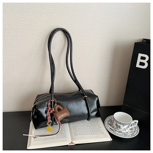 Detail of minimalist black cylindrical underarm bag with decorative mini pouch on an open book
