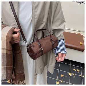 Brown suede bowling bag featuring leather trim and adjustable strap in autumn street setting