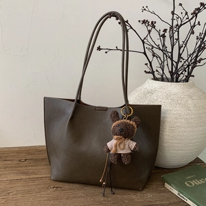 Détail du sac cabas en cuir marron foncé avec texture grainée et pendentif ours