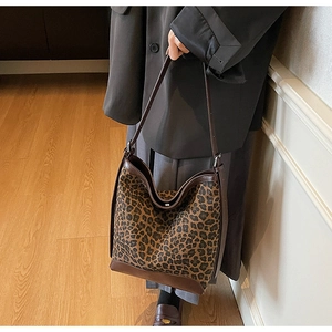 Detail of leopard print tote bag with brown leather trim held by a model in interior