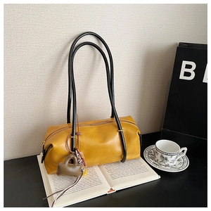 Close-up of bright yellow leather Boston bag with slim black handles and a mini charm detail