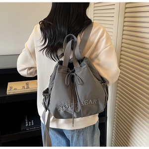 Detail of grey drawstring bucket bag with YOUJI BEAR embroidery on light nylon material