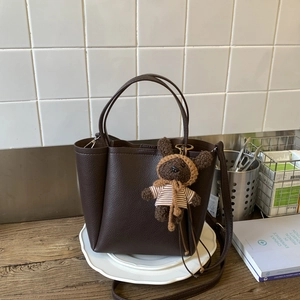 Detail view of brown pebbled leather tote bag with a cute bear charm on a white tray