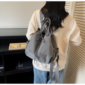 Detail of grey nylon drawstring bucket bag with YOU J BEAR embroidery on model