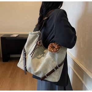 Close-up of olive green tote bag with leather strap detail and plush donut charm