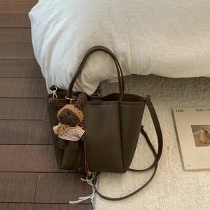 Detail of dark brown pebble leather tote bag featuring a cute knitted bear charm accessory
